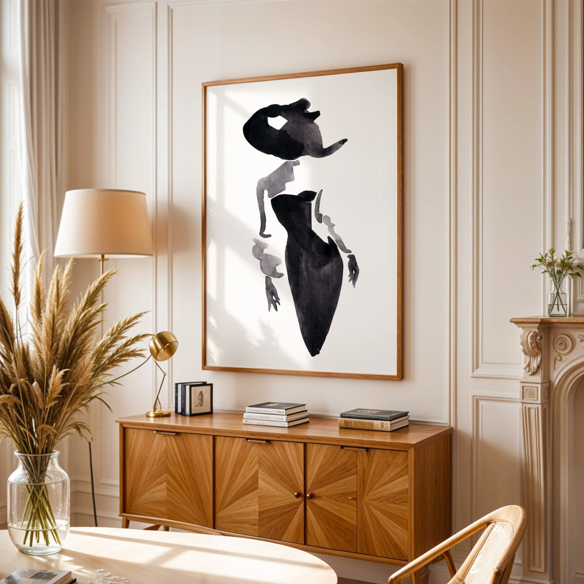 Ink wash woman in fitted black dress print in an oak frame above a sunburst wood sideboard with pampas grass