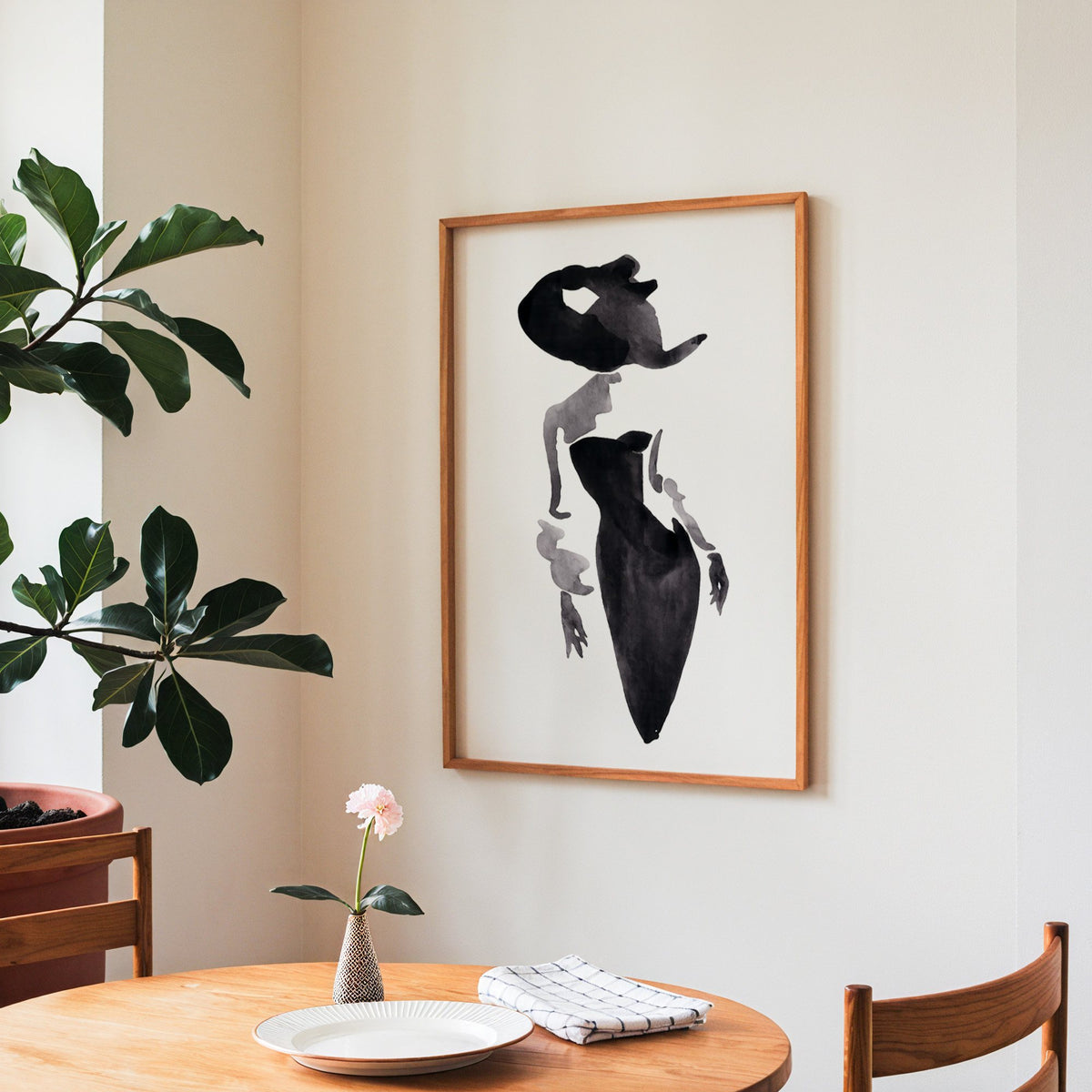 Ink wash woman in fitted black dress print in a teak frame above a round wooden dining table