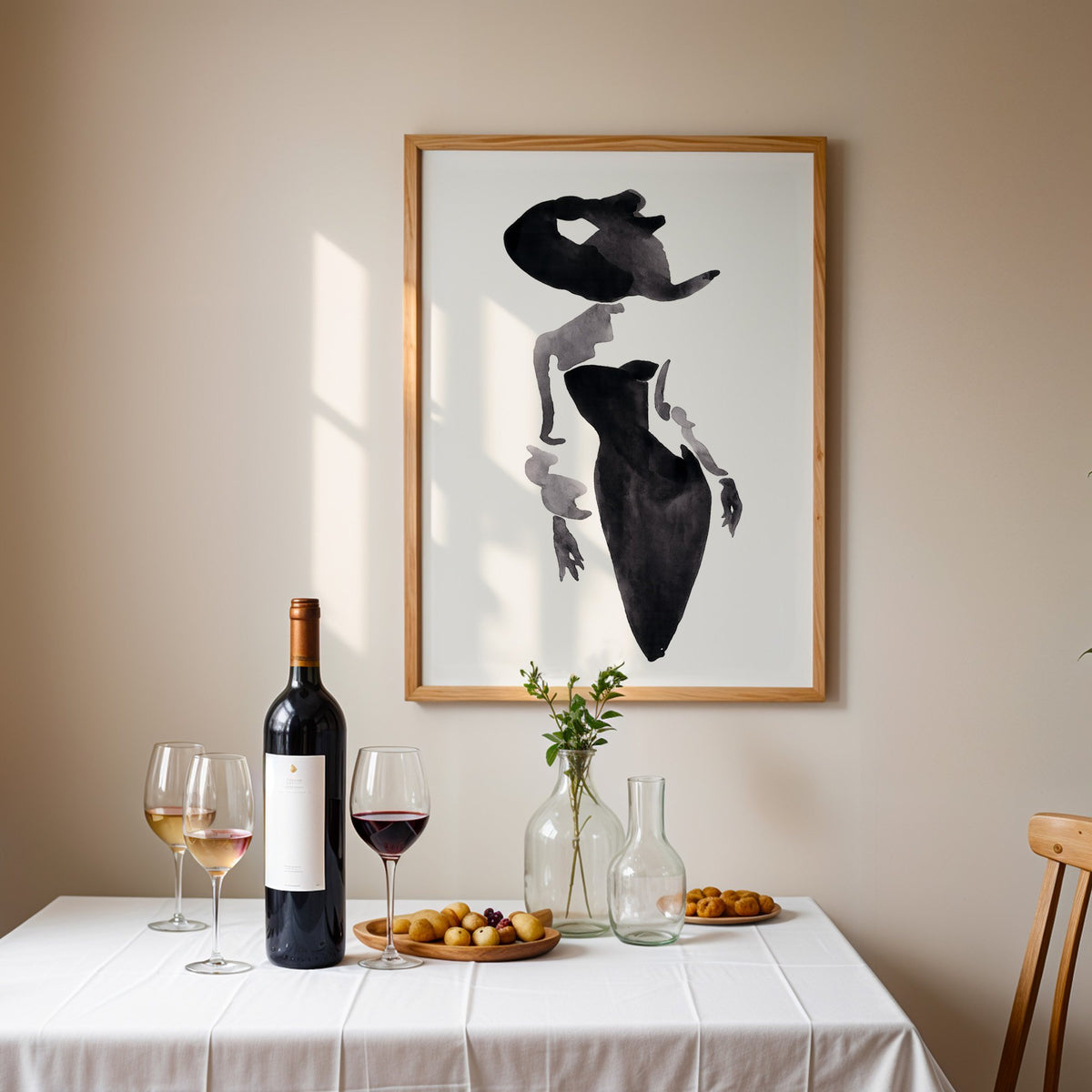 Ink wash woman in fitted black dress print in an oak frame above a table set with red wine and glasses