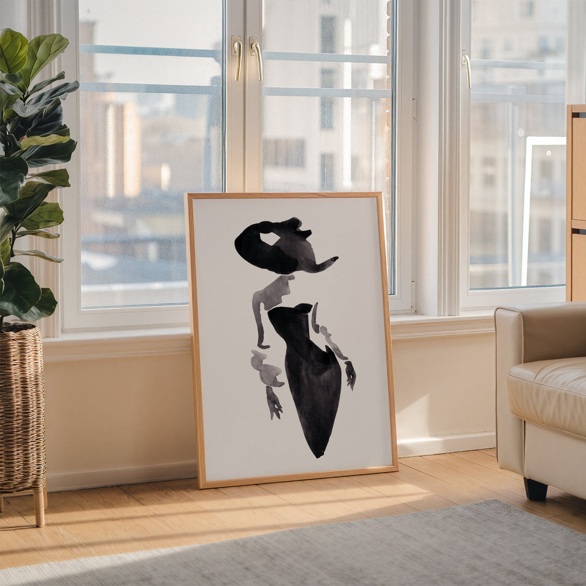 Ink wash woman in fitted black dress print in an oak frame leaning on the floor beside a fiddle leaf fig