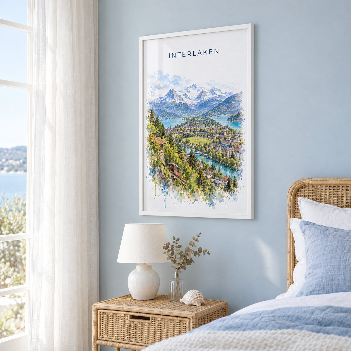 Interlaken watercolor print in a white frame on a pale blue wall beside a rattan bed in a coastal bedroom