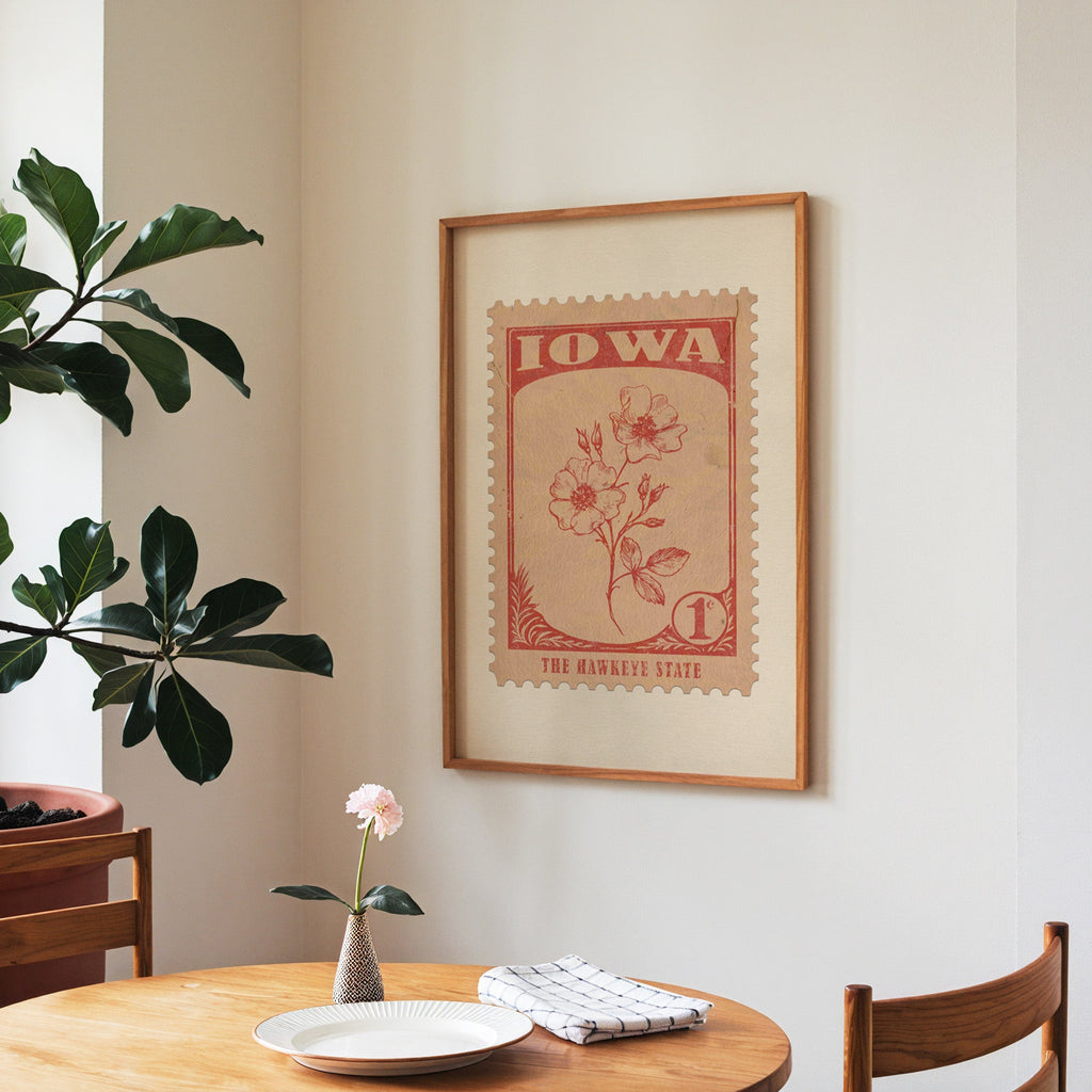 Iowa state flower print framed above a round wooden table with a single bloom in a vase and books