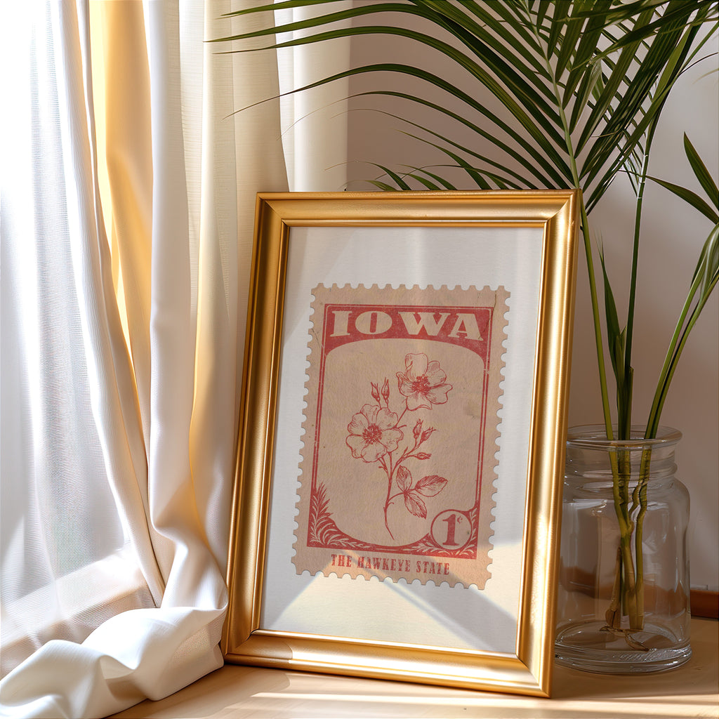Iowa stamp print in a gold frame leaning by a cream curtain with a palm in a glass jar