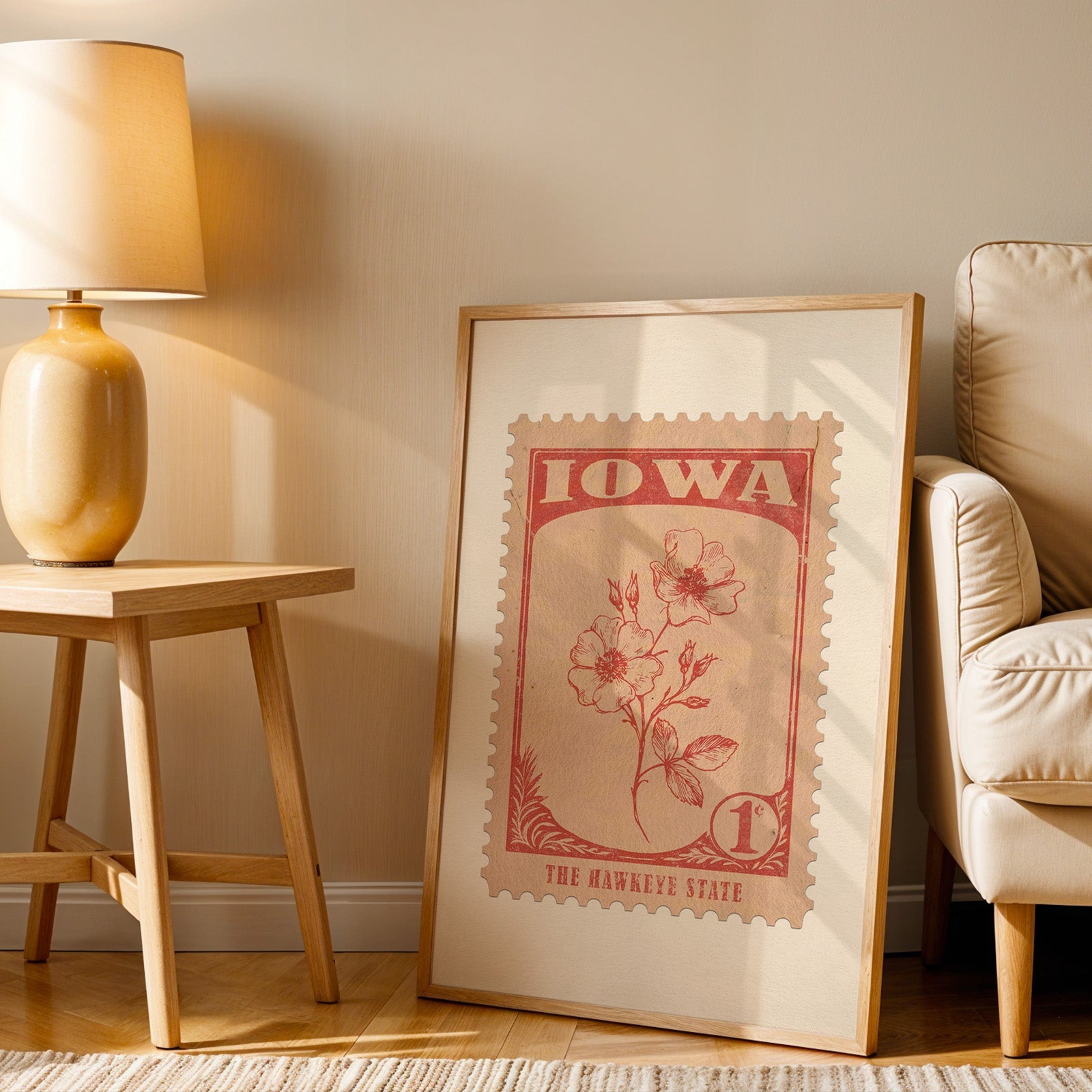 Iowa stamp print in a wood frame resting on the floor beside a beige armchair and a yellow lamp