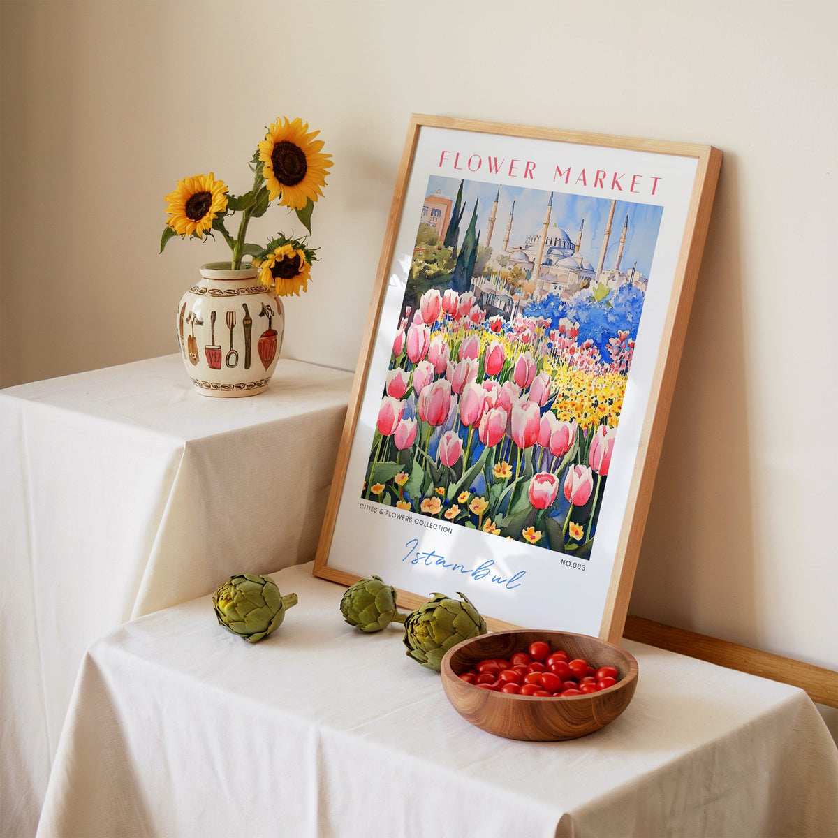 Istanbul flower market print in an oak frame leaning on a linen-draped table beside a vase of sunflowers