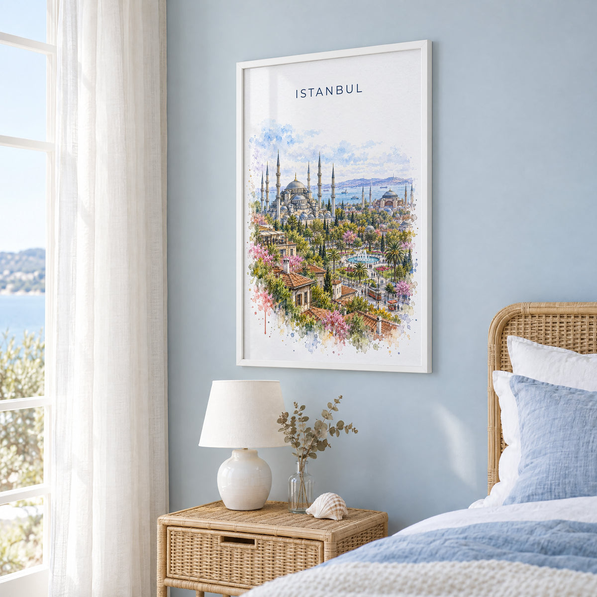 Istanbul watercolor print in a white frame on a pale blue wall beside a rattan bed in a coastal bedroom