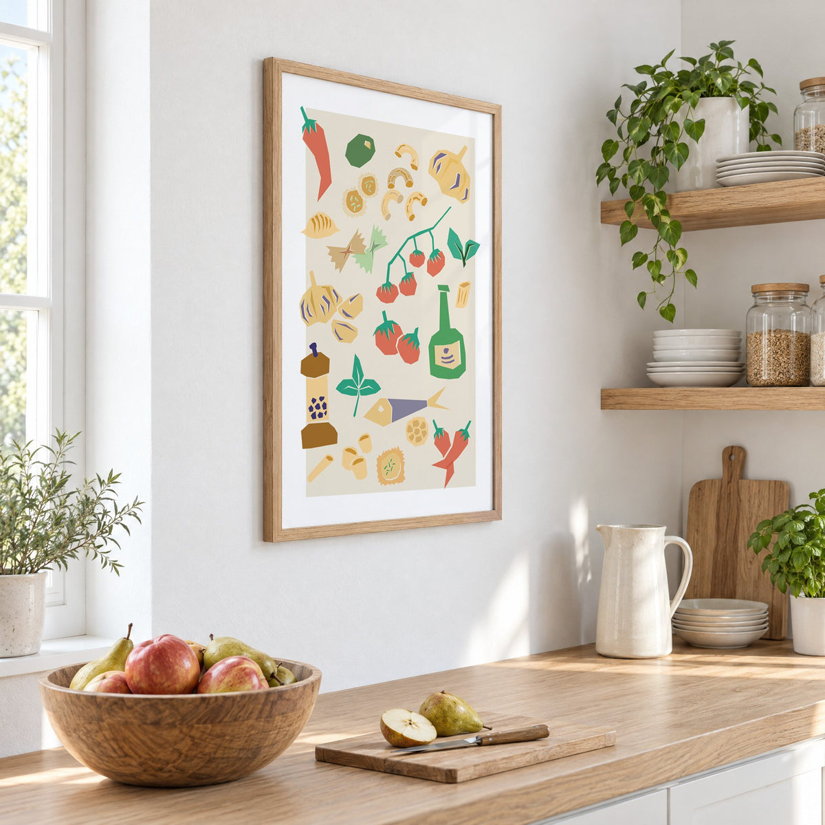 Italian ingredients cut-paper pattern print in an oak frame on a white kitchen wall above a counter with apples and pears, seen at an angle