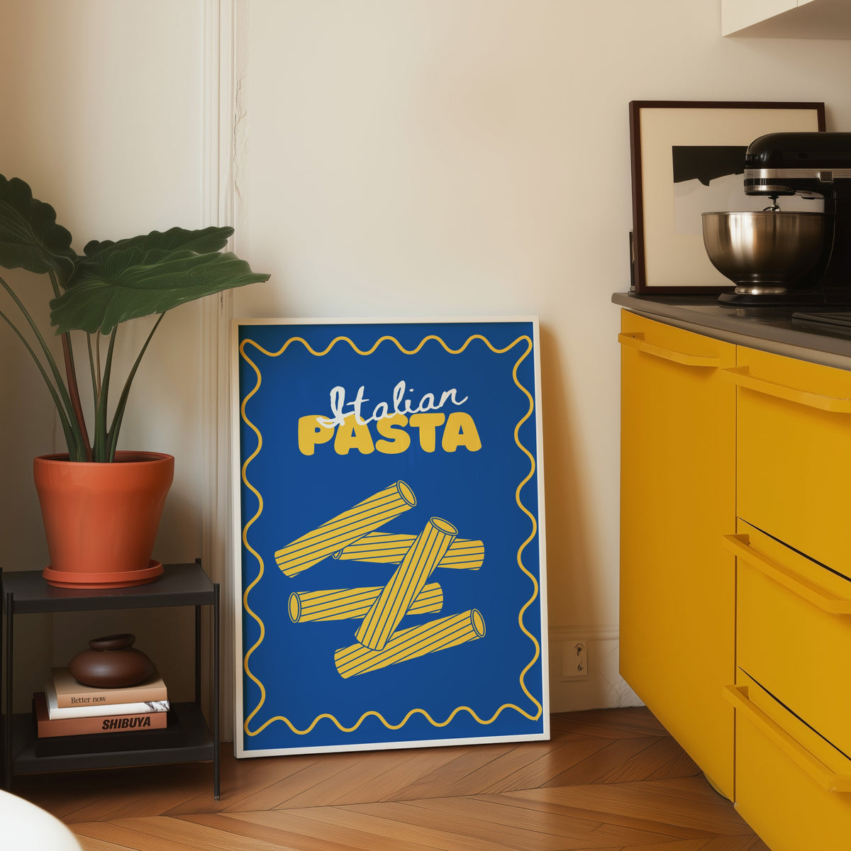 Navy rigatoni print in a white frame leaning on parquet beside a yellow kitchen