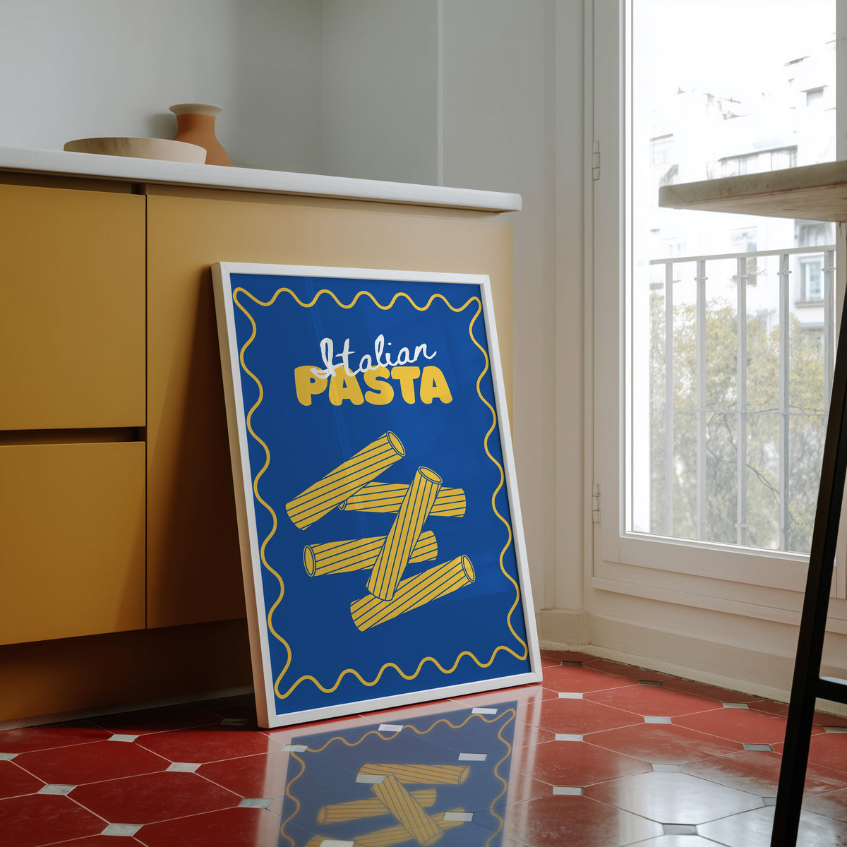 Navy rigatoni print in a white frame against yellow cabinets on a red tiled floor