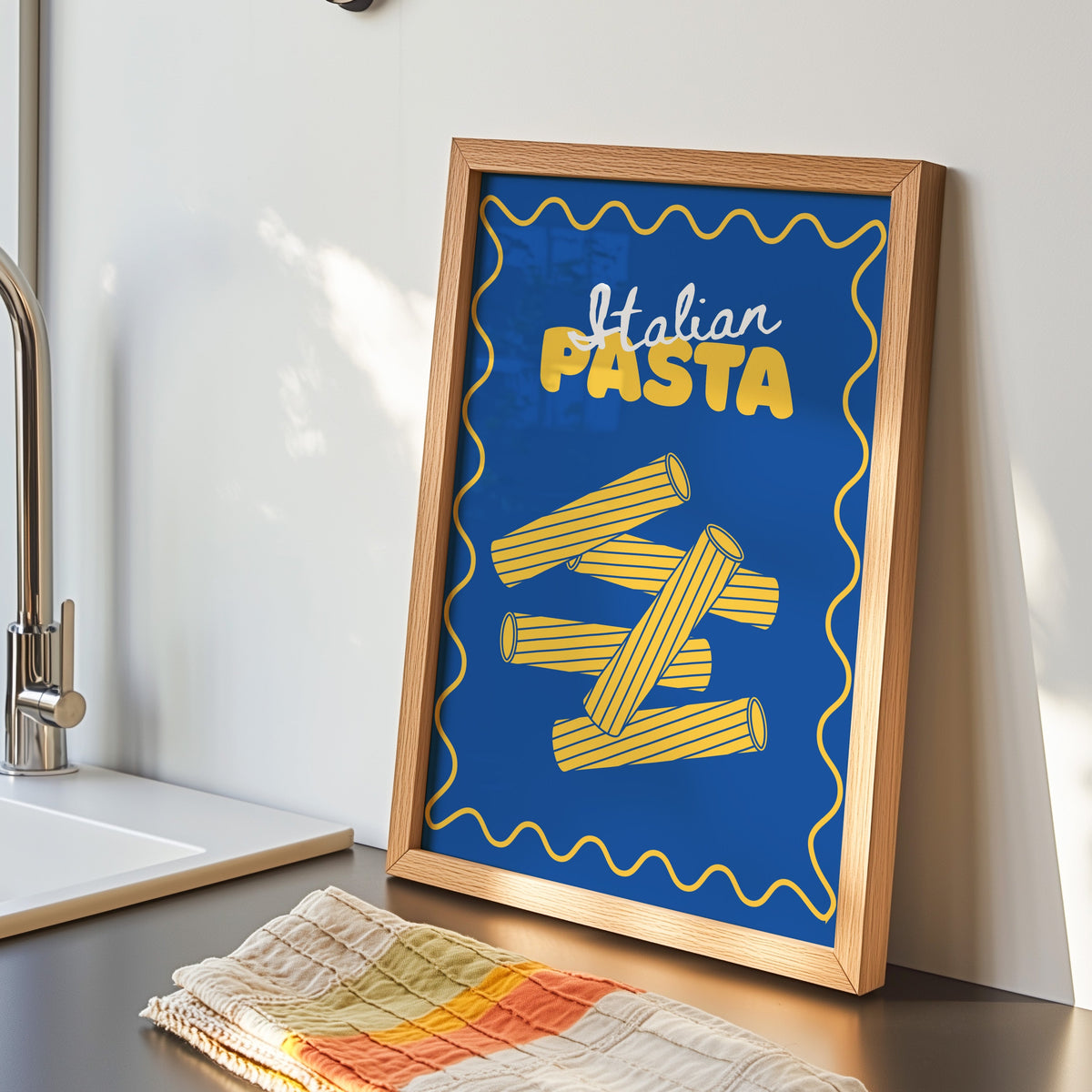 Navy rigatoni print in an oak frame by the kitchen sink beside a striped tea towel