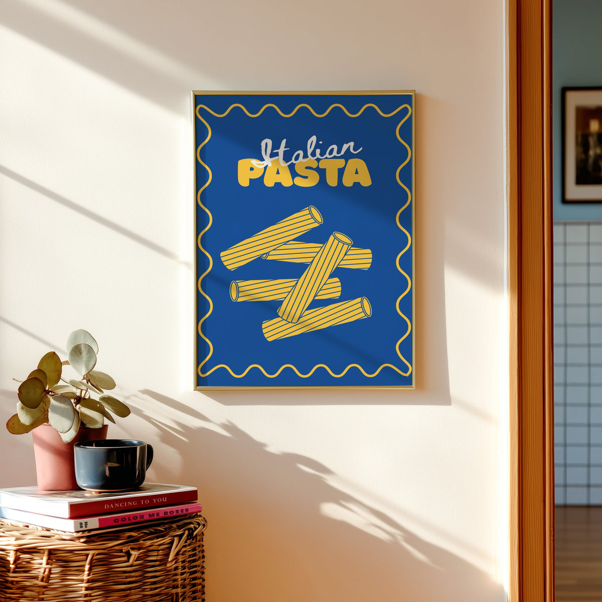 Navy rigatoni print in a gold frame above a basket of books and a pilea plant