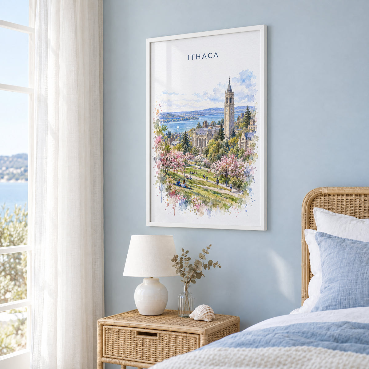 Ithaca watercolor print in a white frame on a pale blue wall beside a rattan bed in a coastal bedroom