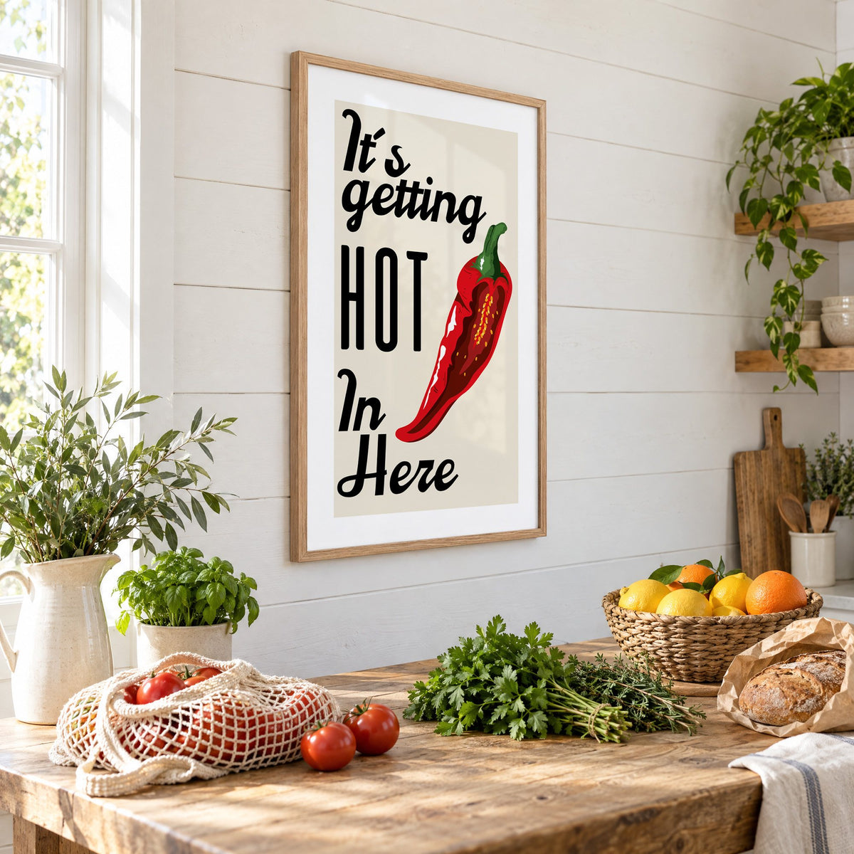 It's getting HOT In Here split chili print in an oak frame on a shiplap wall above a farm table with market tomatoes and citrus, seen at an angle