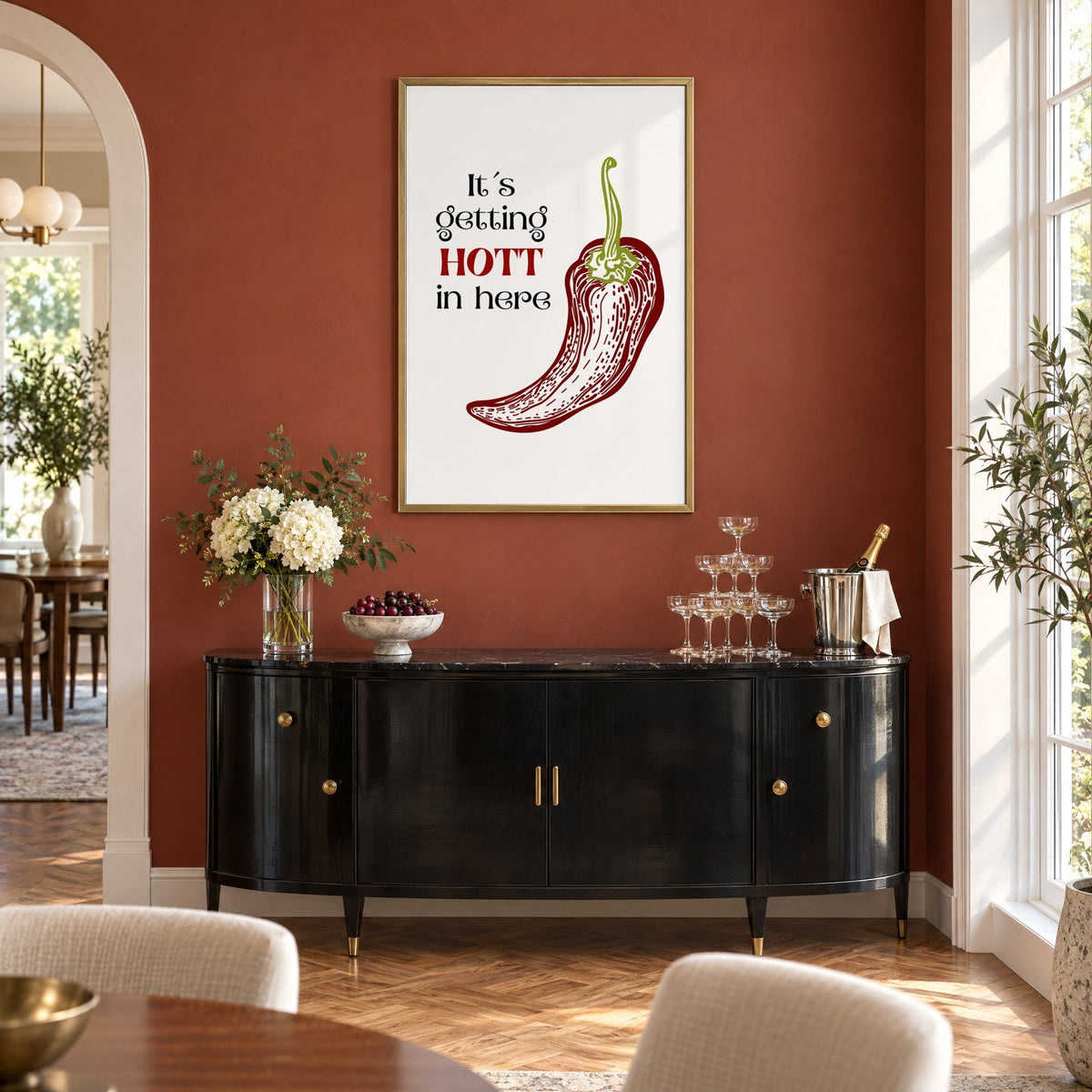 It's getting HOTT red chili print in a brass frame on a terracotta wall above a black buffet with a champagne tower