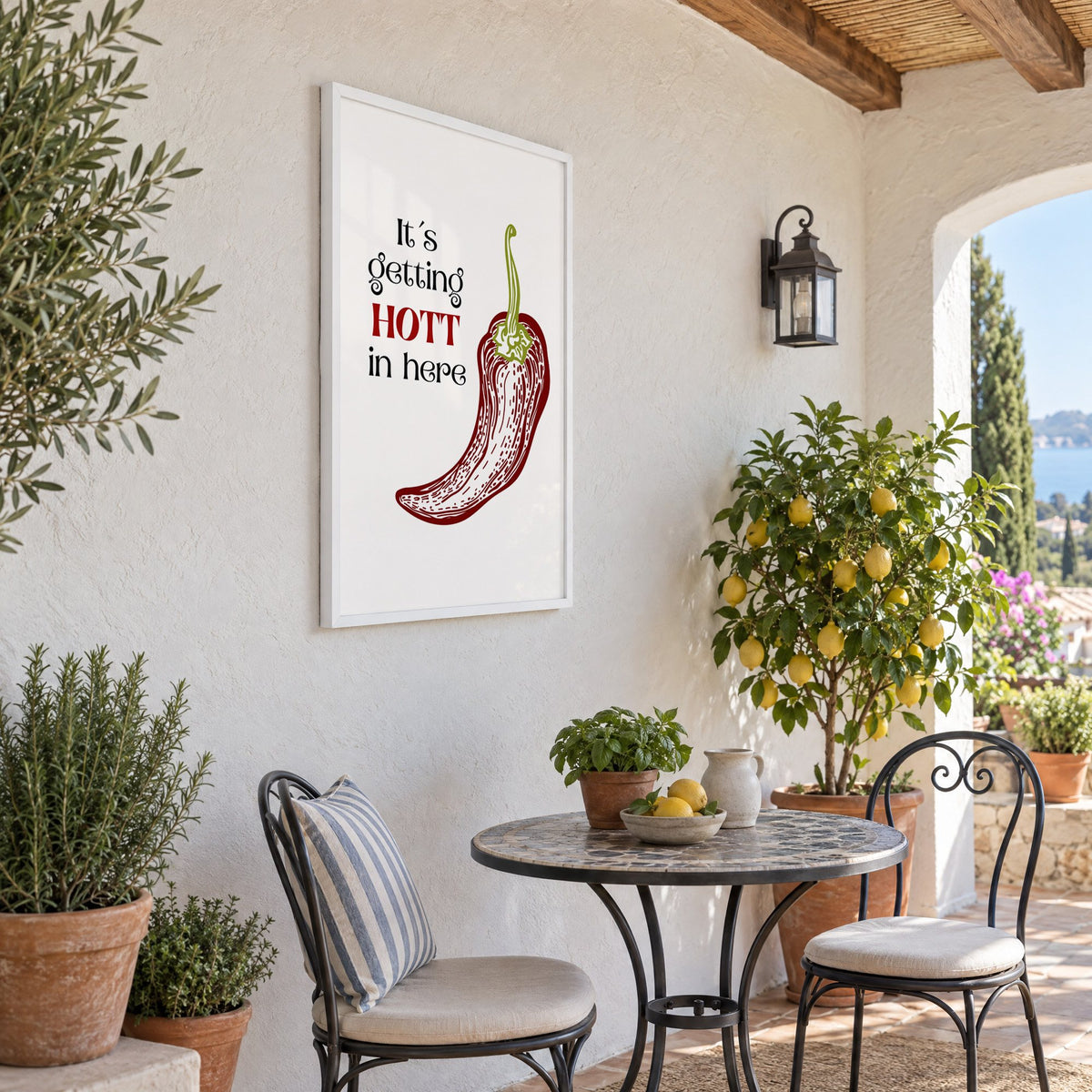 It's getting HOTT red chili print in a white frame on a sunny patio wall beside a potted lemon tree