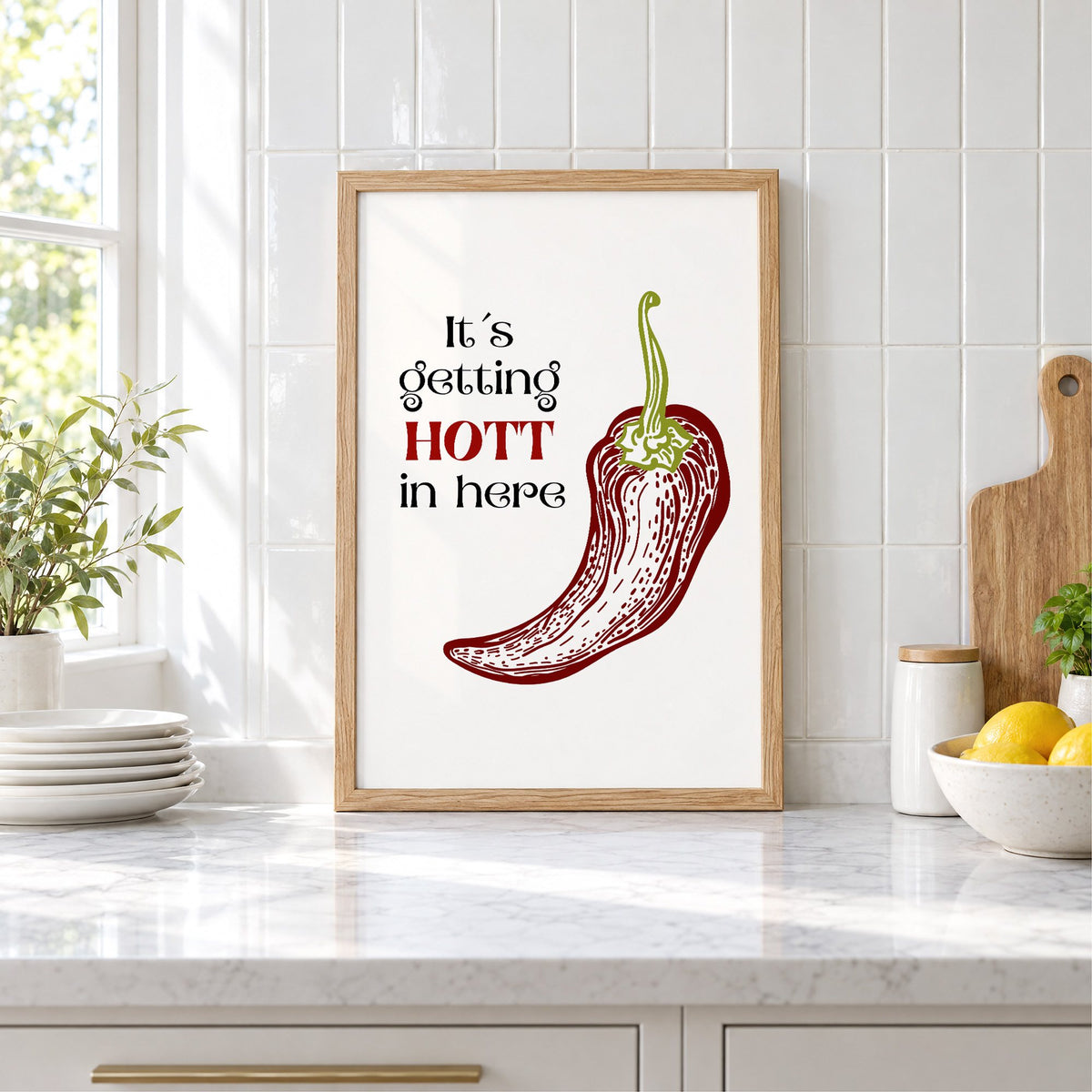 It's getting HOTT red chili print in an oak frame leaning on a marble counter by white tiles and lemons