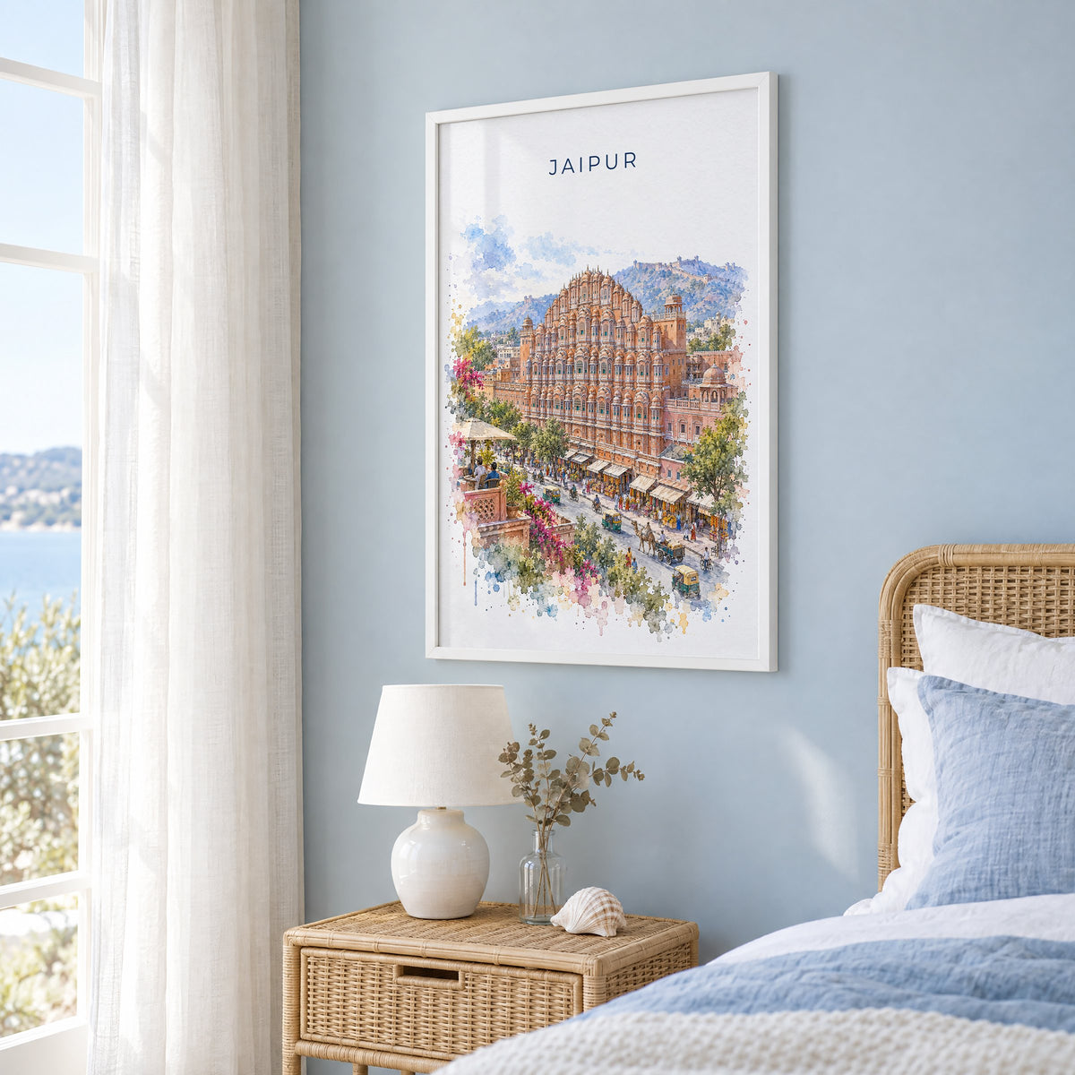 Jaipur watercolor print in a white frame on a pale blue wall beside a rattan bed in a coastal bedroom