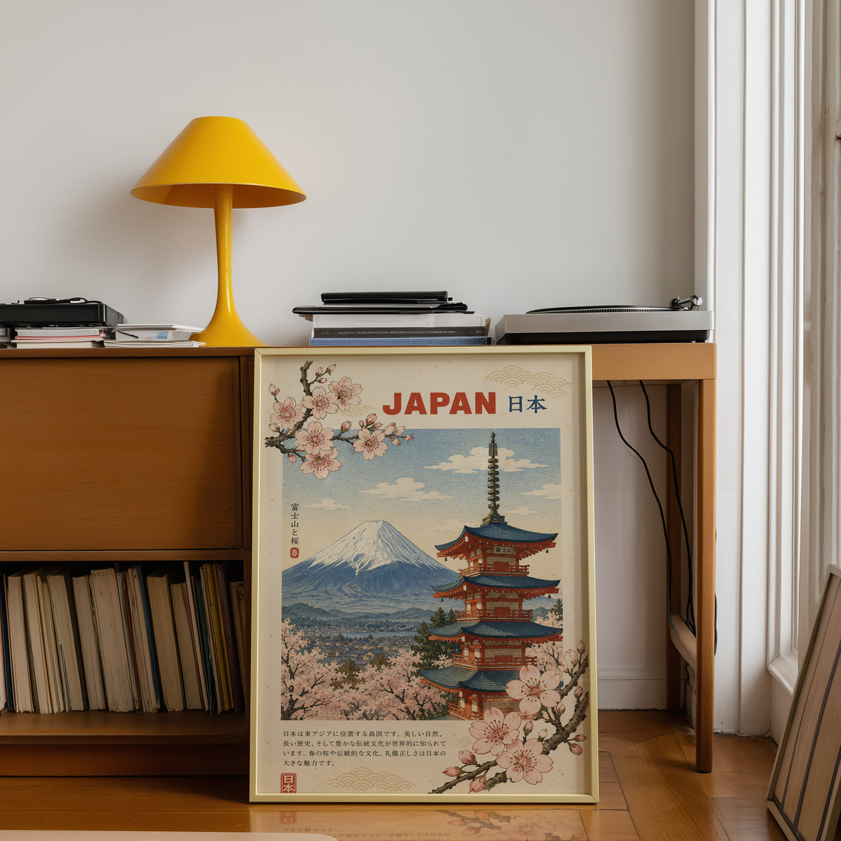 Mount Fuji, red pagoda and sakura print shown in a gold frame leaning under a teak desk with a yellow lamp