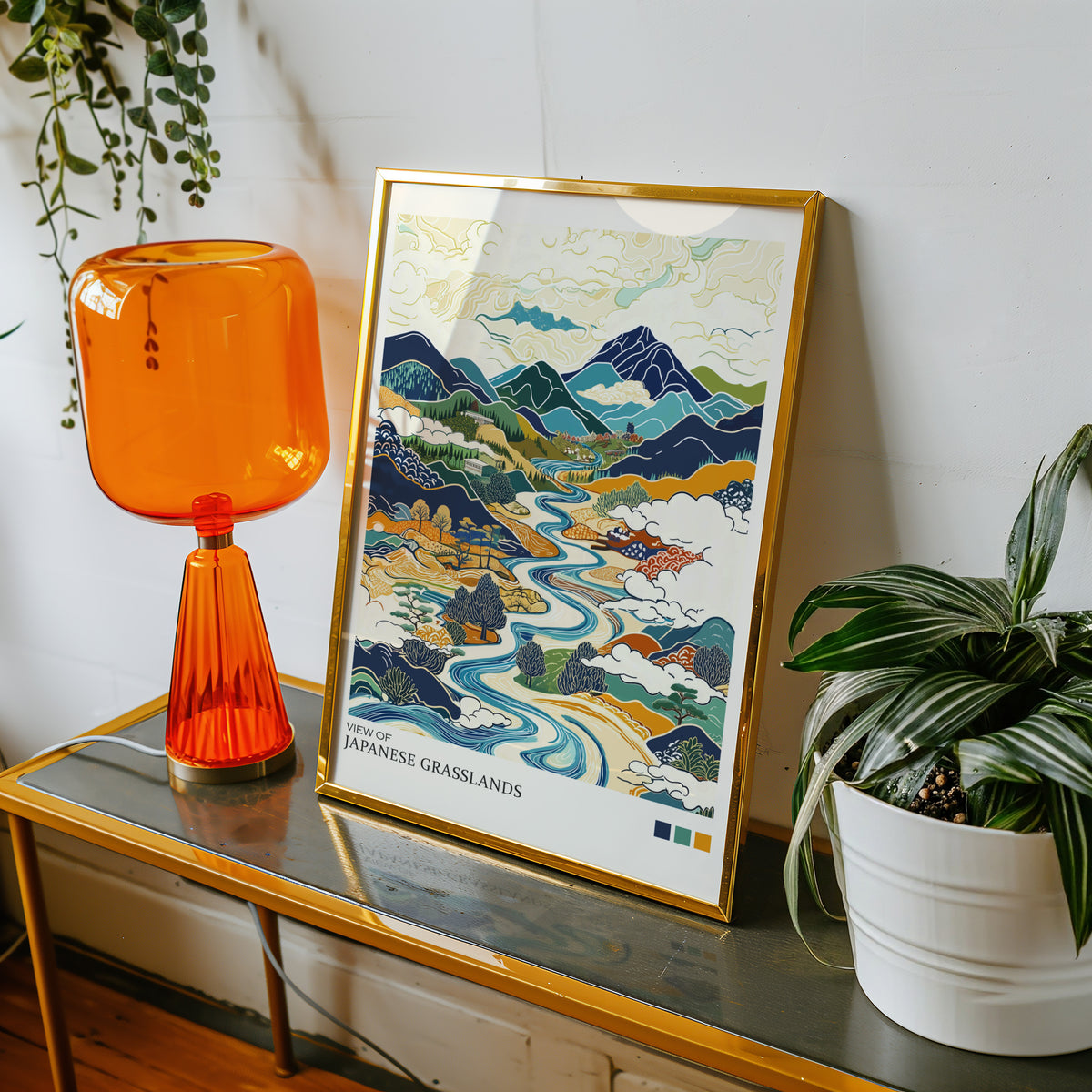 View of Japanese Grasslands river valley print shown in a gold frame on a console beside an orange glass lamp