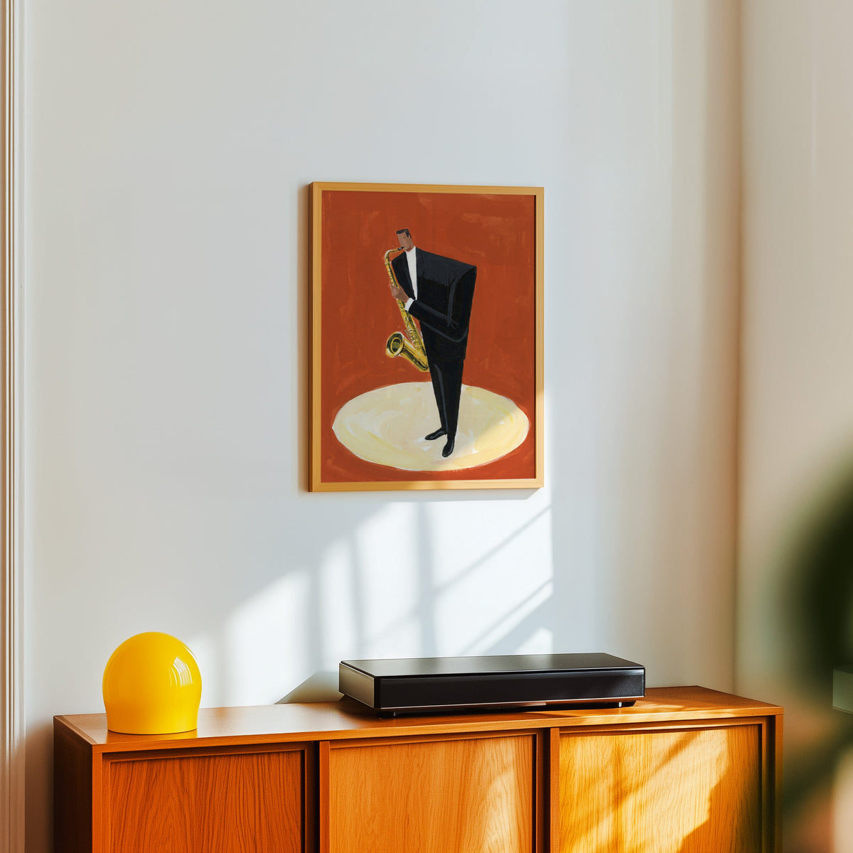 Red jazz club print in a light oak frame above a teak sideboard with a yellow lamp