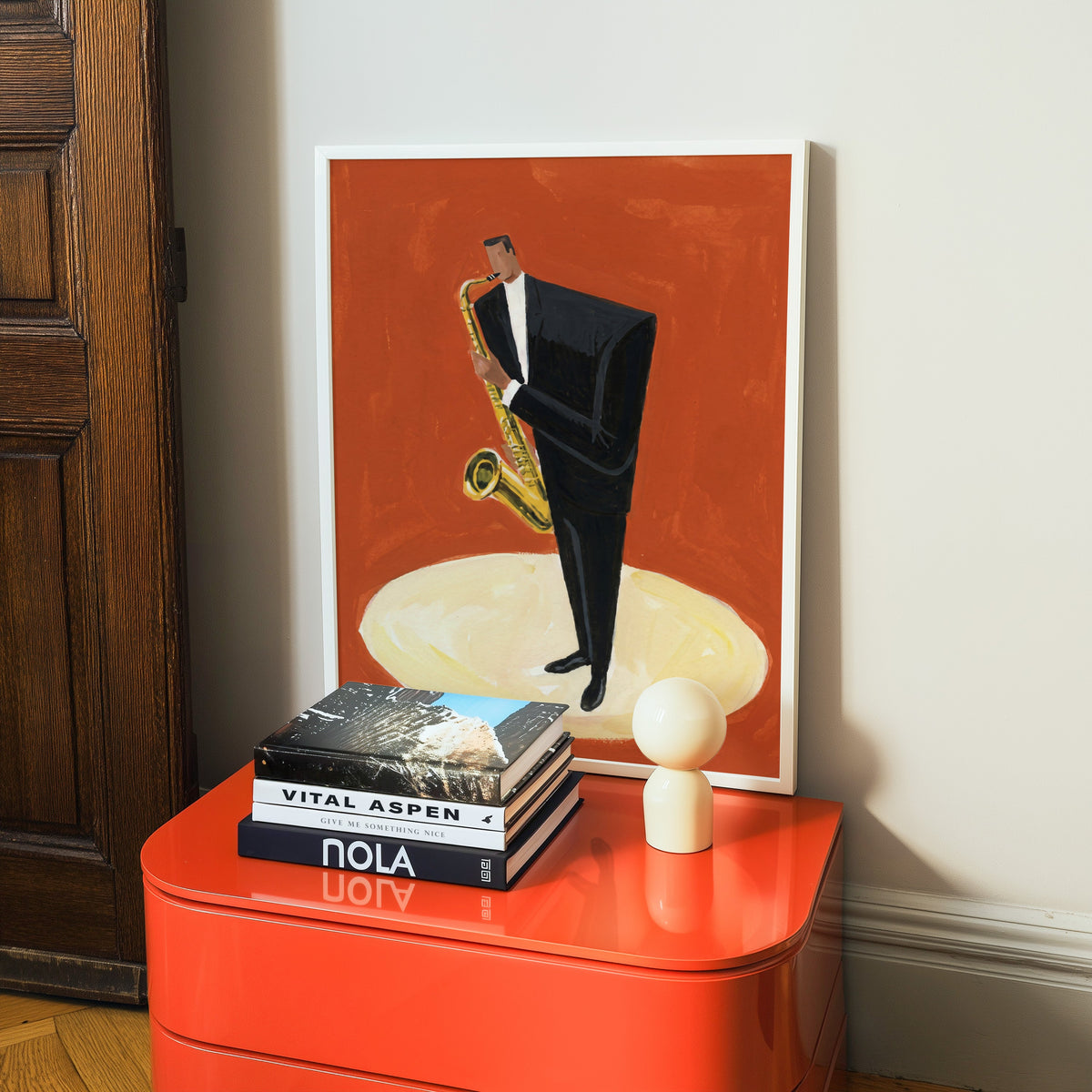Mid century jazz print in a white frame on a glossy orange cabinet with books