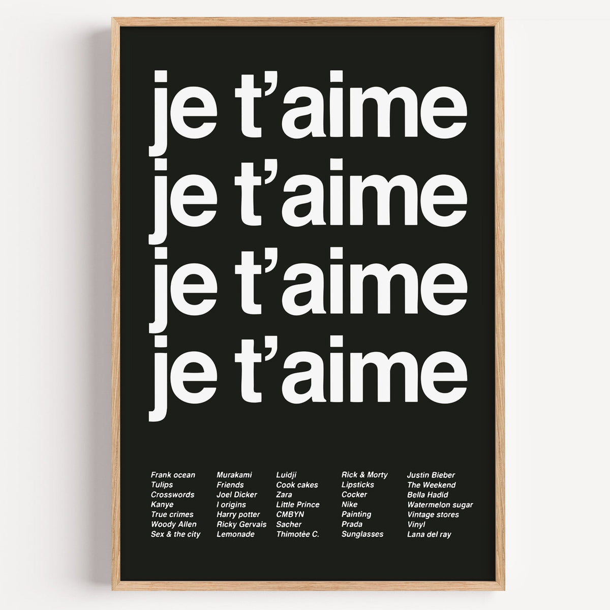 Je t'aime four-line typography with small list print in a light oak frame on a plain white wall