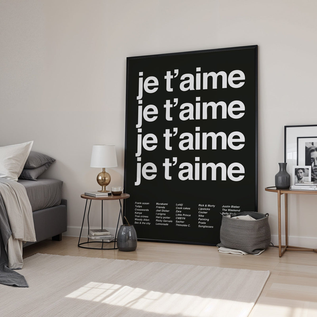 Je t'aime four-line typography with small list print in a black frame leaning in a bedroom beside a gold lamp