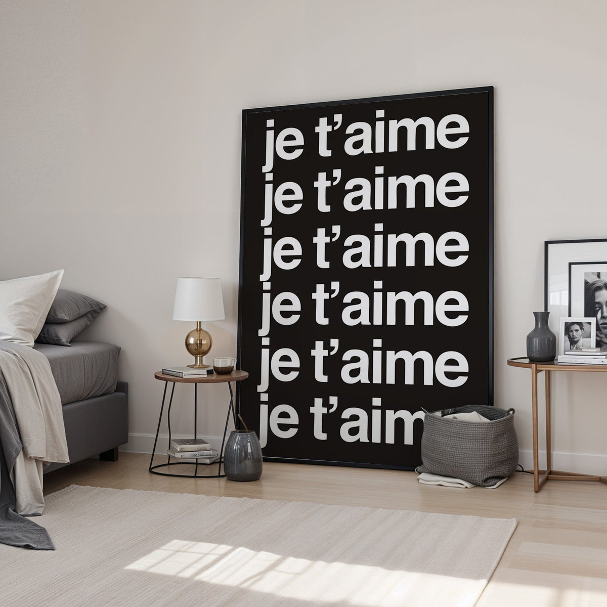 Je t'aime repeated six times in white type print in a black frame leaning in a bedroom beside a gold lamp