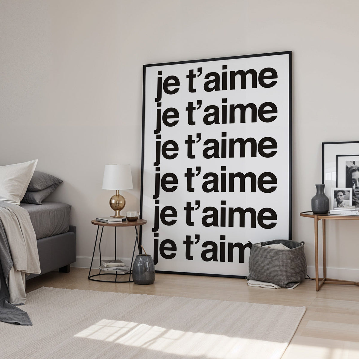 Je t'aime repeated six times in black type print in a black frame leaning in a bedroom beside a gold lamp
