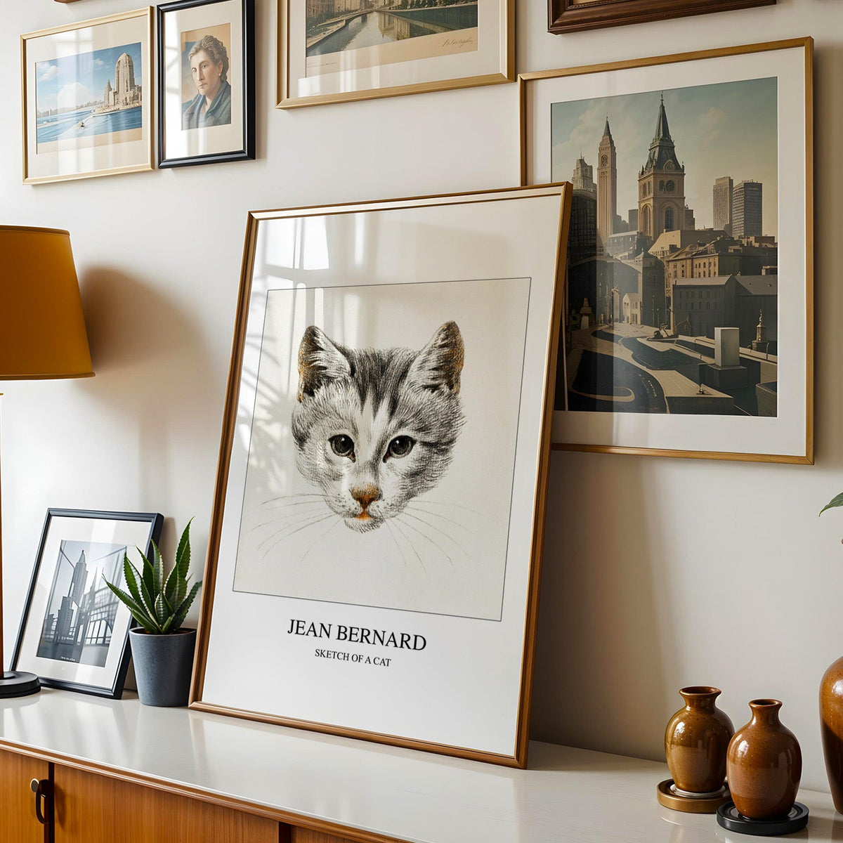 Kitten print shown in a gold frame leaning on a sideboard in a gallery wall