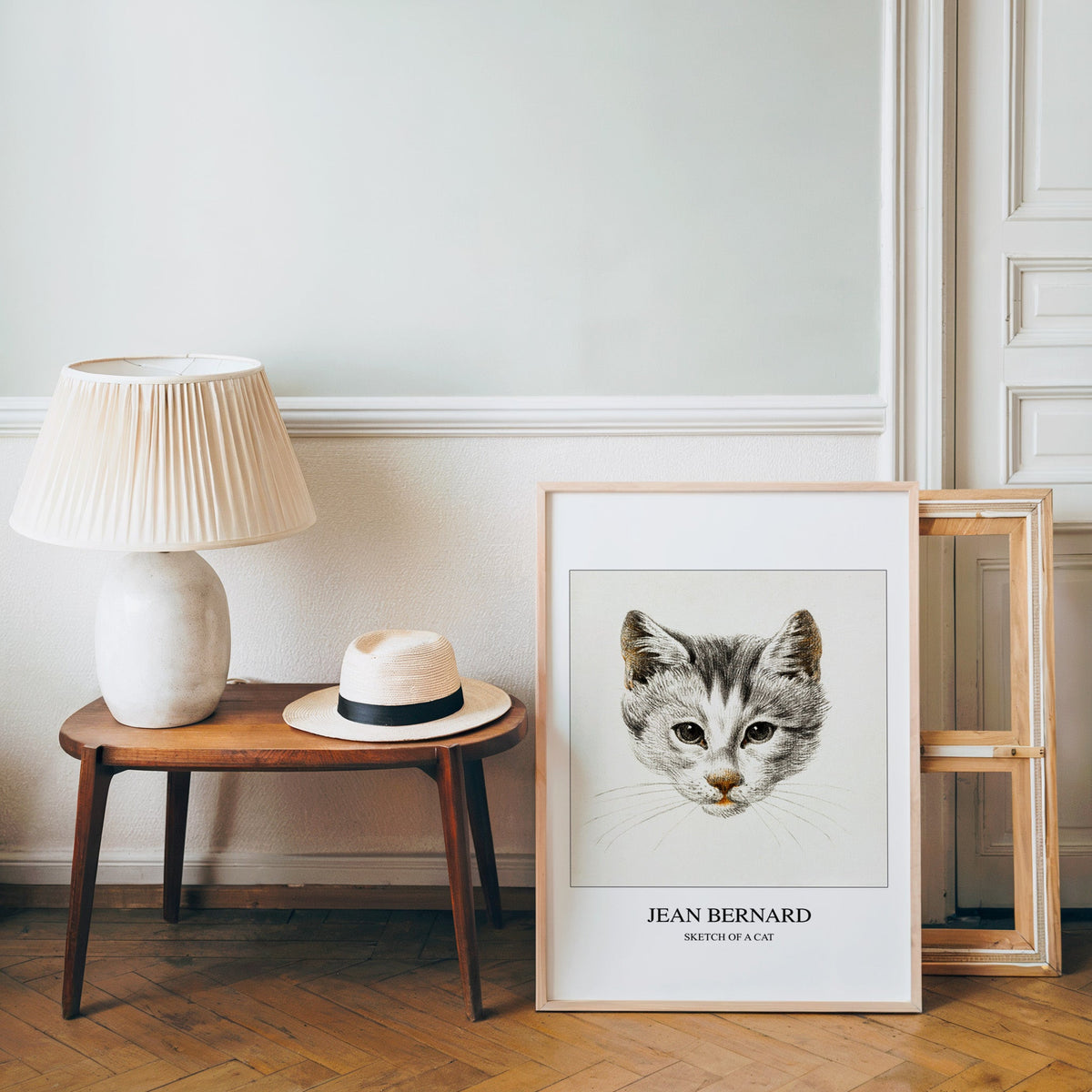 Kitten drawing poster in a light wood frame leaning by a bench and panama hat
