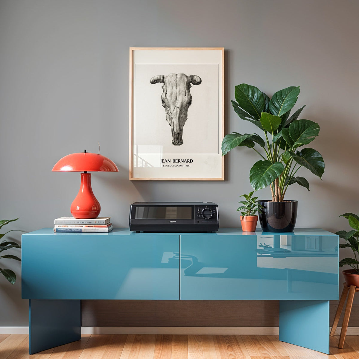 Skull study print in an oak frame above a teal sideboard with a red lamp