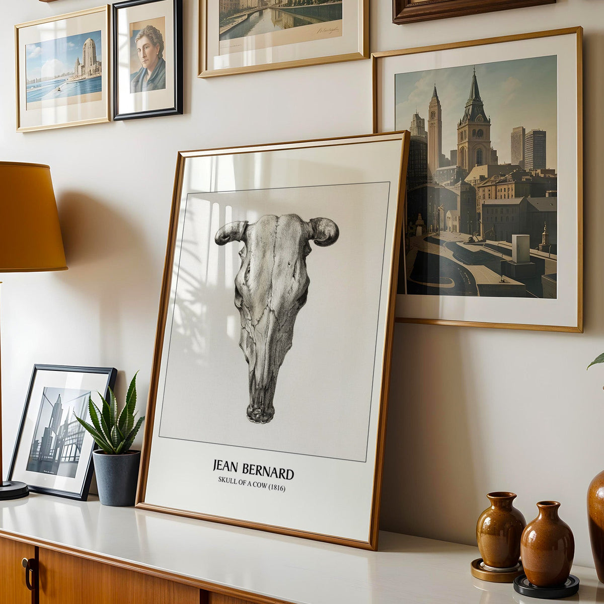 Skull drawing shown in a gold frame leaning on a sideboard in a gallery wall