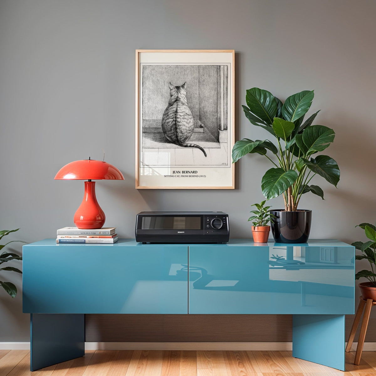 Pencil cat print in an oak frame above a teal sideboard with a red lamp