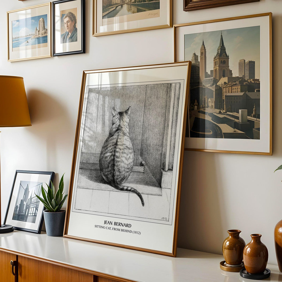 Cat drawing shown in a gold frame leaning on a sideboard in a gallery wall