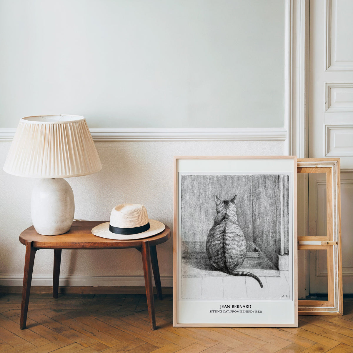 Vintage cat poster in a light wood frame leaning by a bench and panama hat