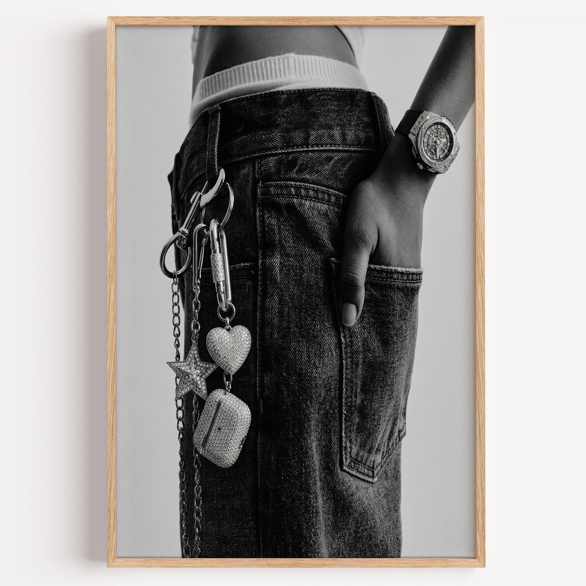 Black jeans with charm chain and jewelled watch print in a light oak frame on a plain white wall
