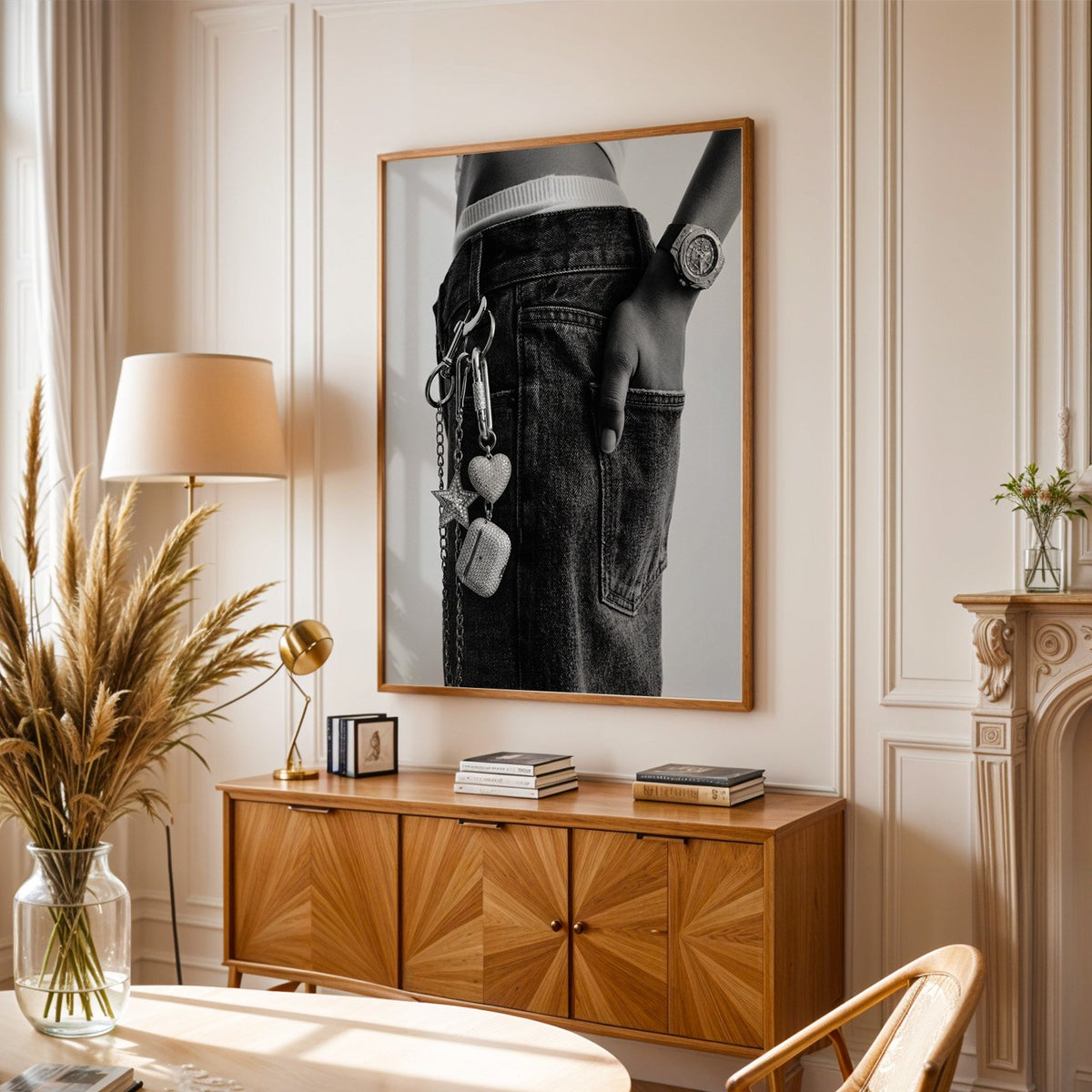 Black jeans with charm chain and jewelled watch print in an oak frame above a sunburst wood sideboard with pampas grass