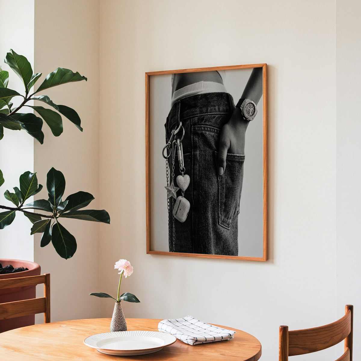 Black jeans with charm chain and jewelled watch print in a teak frame above a round wooden dining table