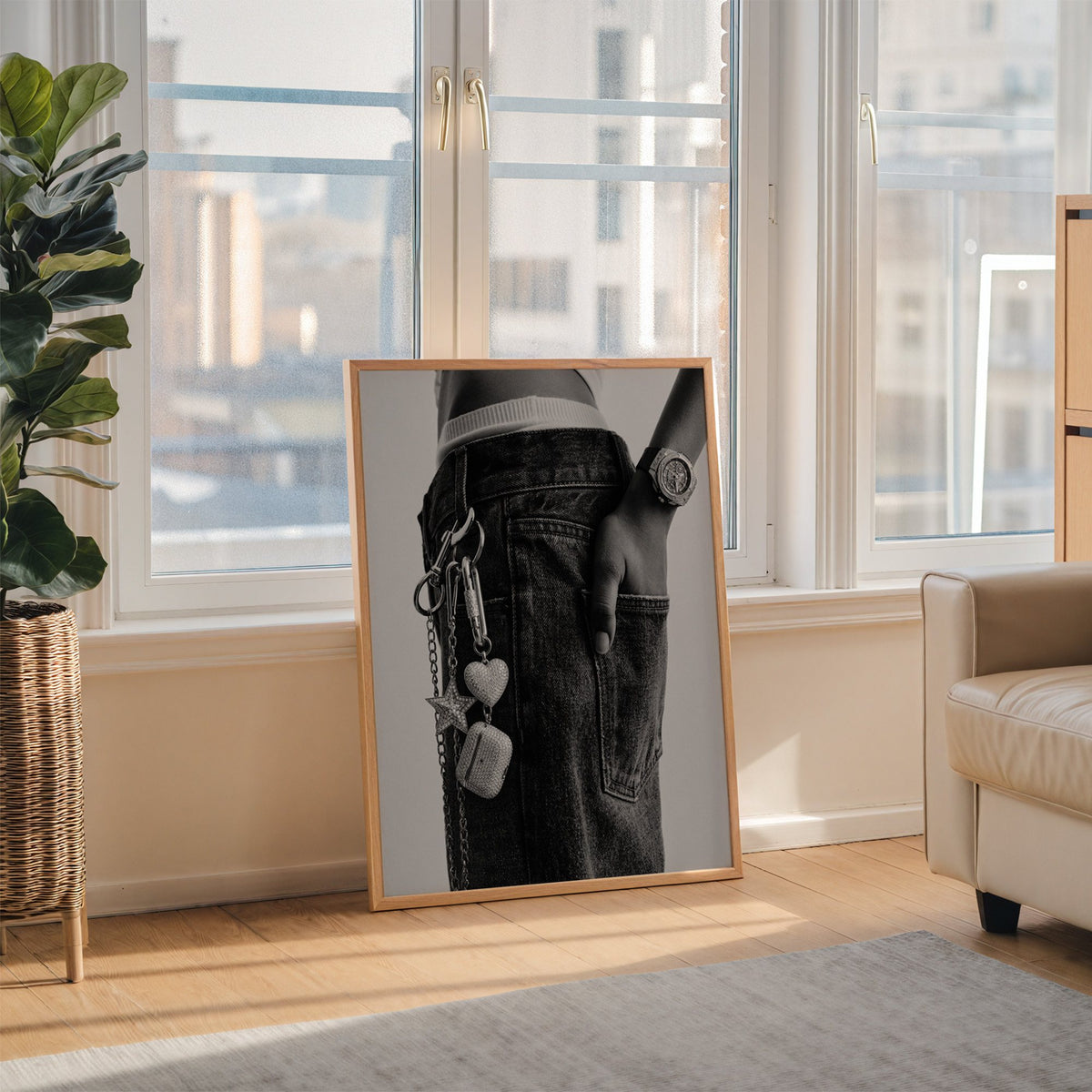 Black jeans with charm chain and jewelled watch print in an oak frame leaning on the floor beside a fiddle leaf fig