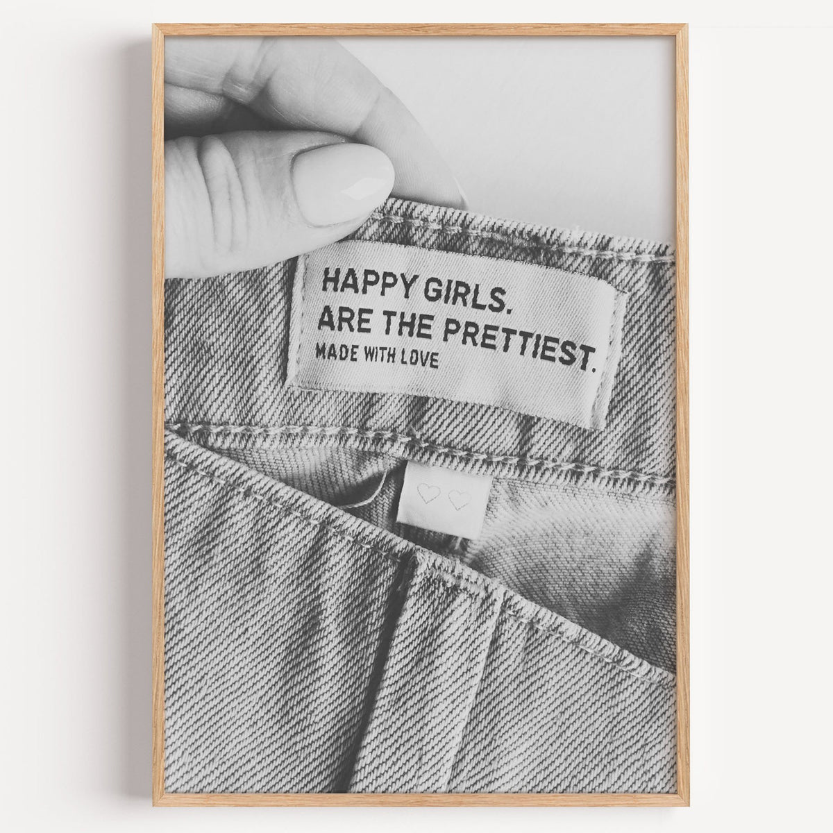 Woven jeans label with Happy Girls quote print in a light oak frame on a plain white wall