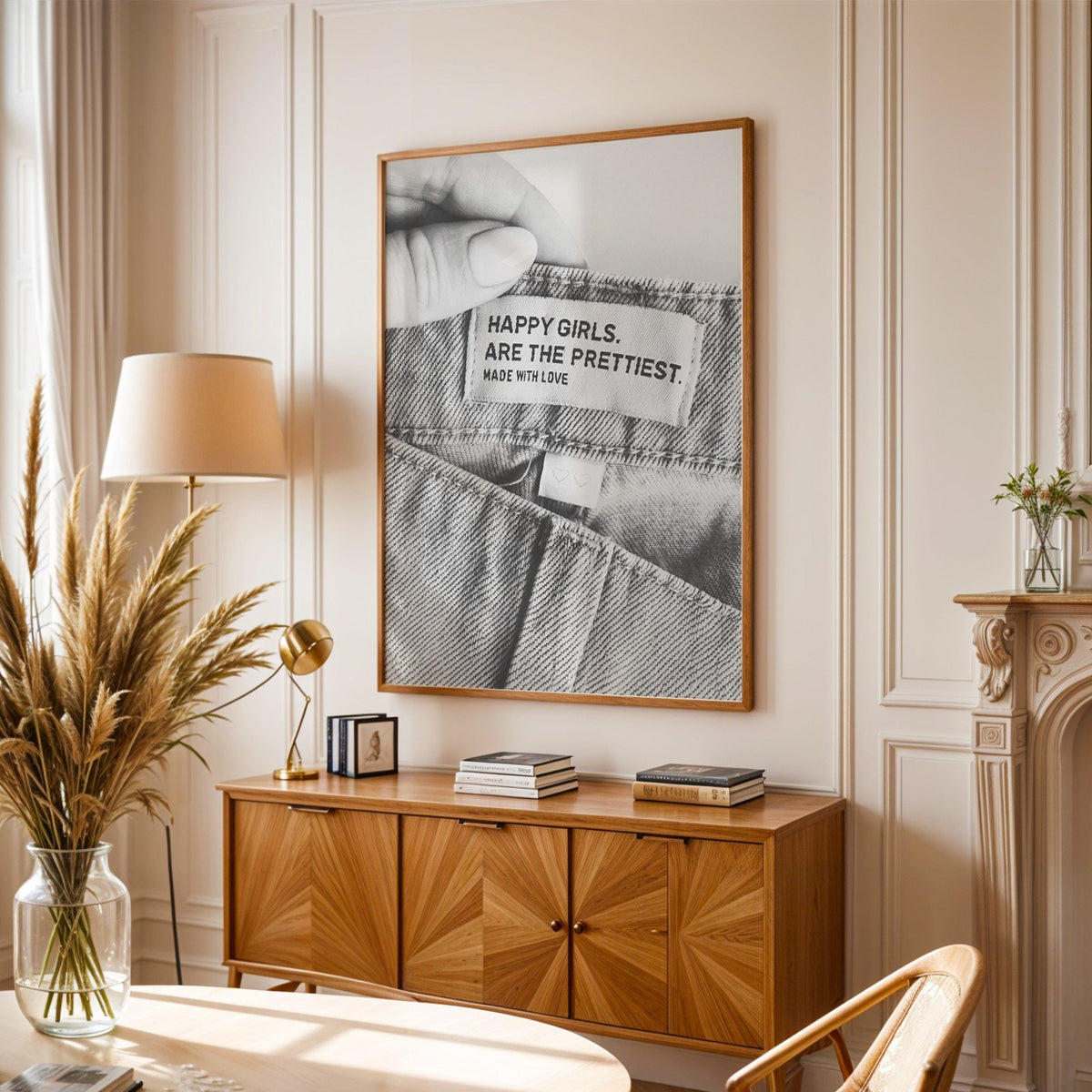 Woven jeans label with Happy Girls quote print in an oak frame above a sunburst wood sideboard with pampas grass