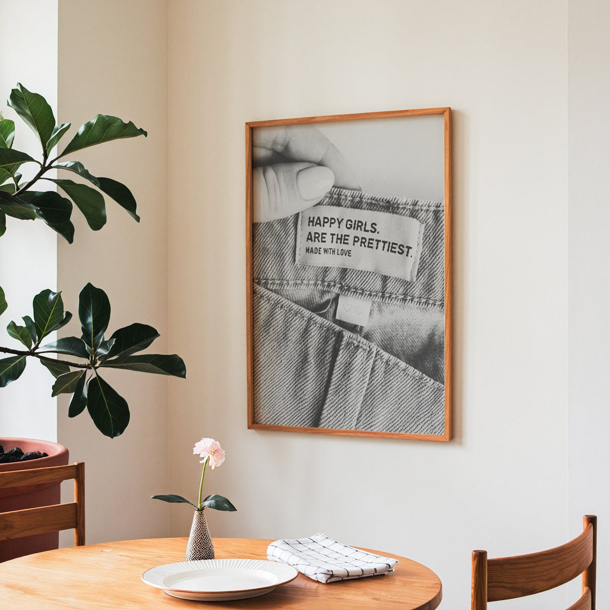 Woven jeans label with Happy Girls quote print in a teak frame above a round wooden dining table