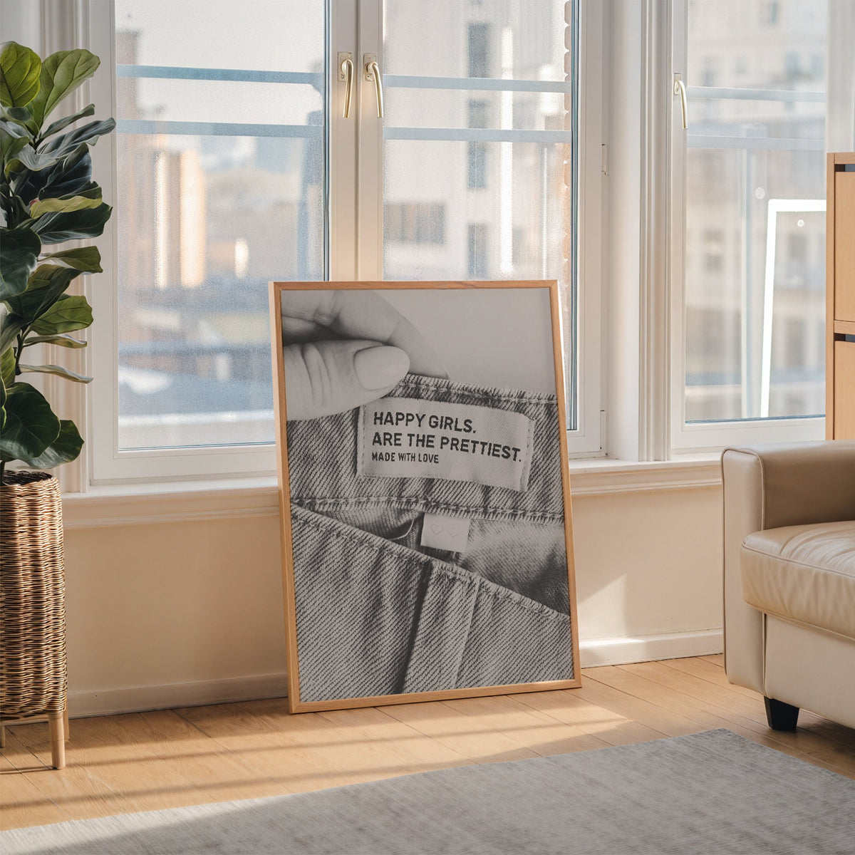 Woven jeans label with Happy Girls quote print in an oak frame leaning on the floor beside a fiddle leaf fig