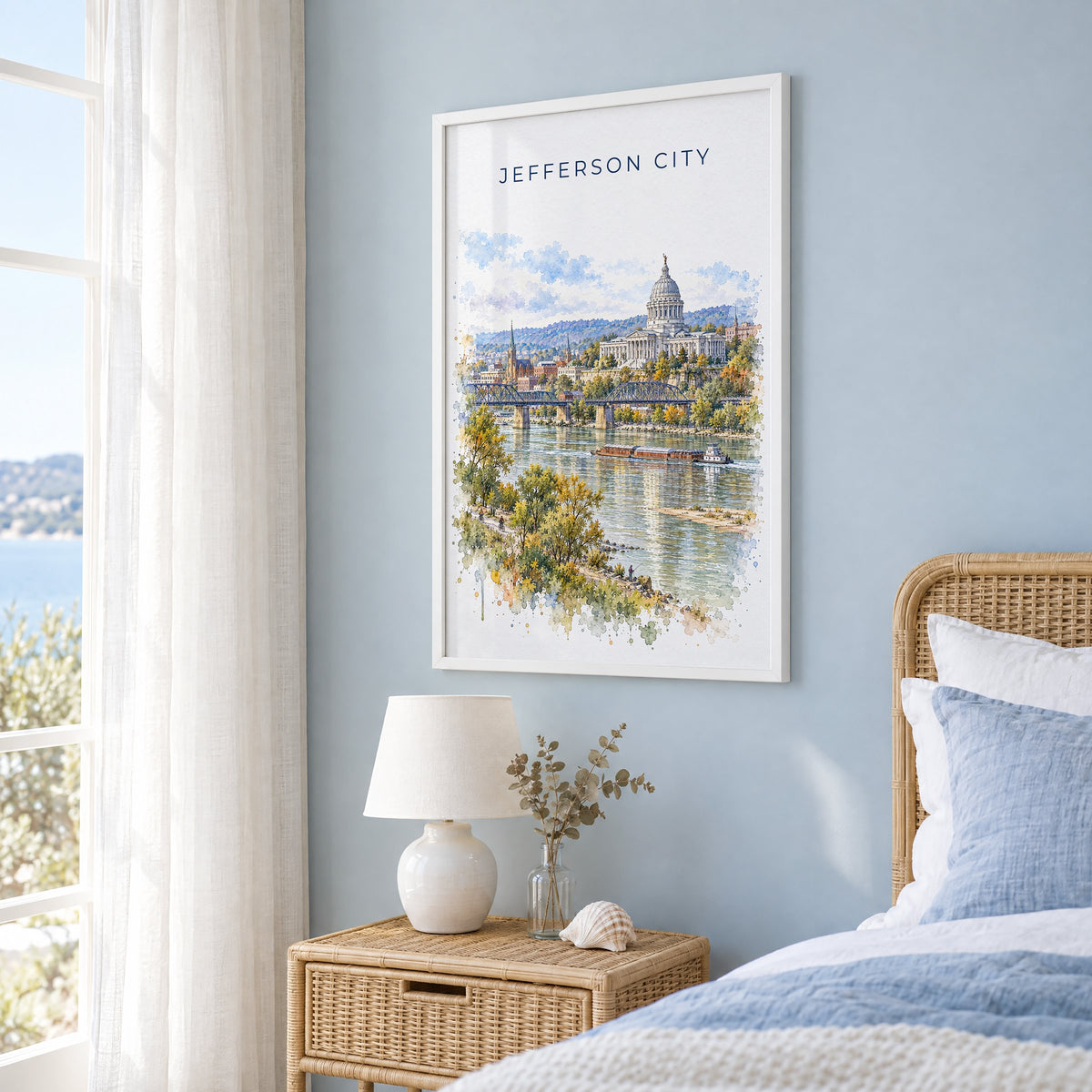 Jefferson City watercolor print in a white frame on a pale blue wall beside a rattan bed in a coastal bedroom