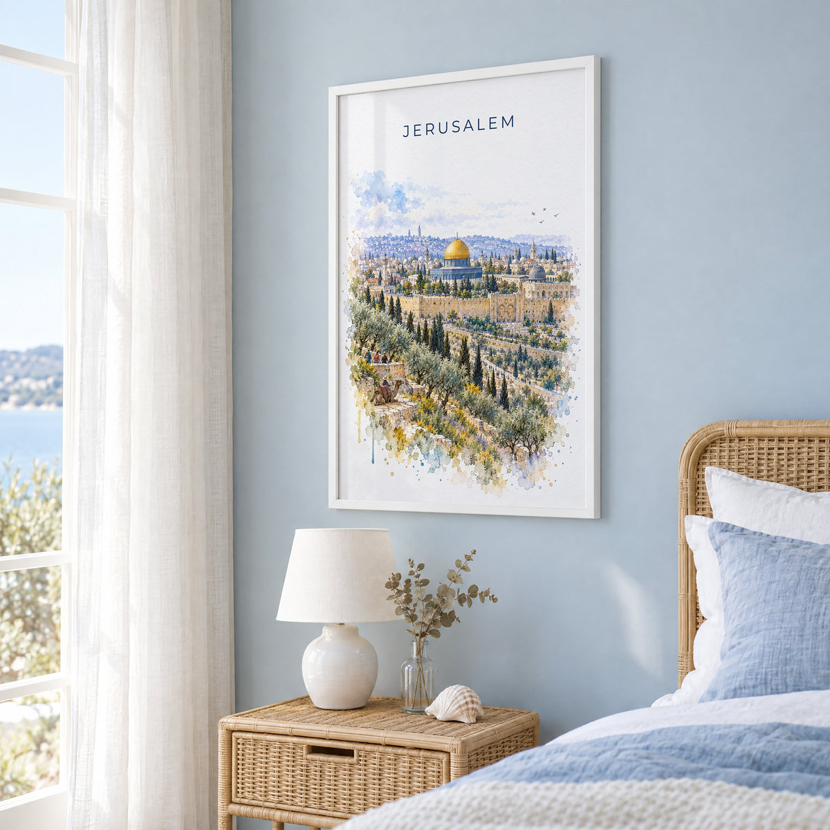 Jerusalem watercolor print in a white frame on a pale blue wall beside a rattan bed in a coastal bedroom