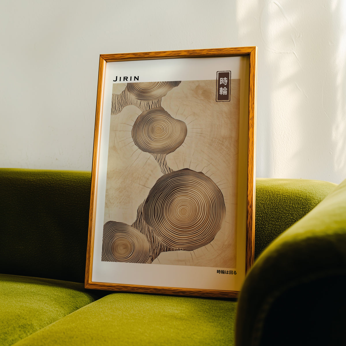 Stacked beige tree ring slices print in an oak frame propped on a green velvet sofa