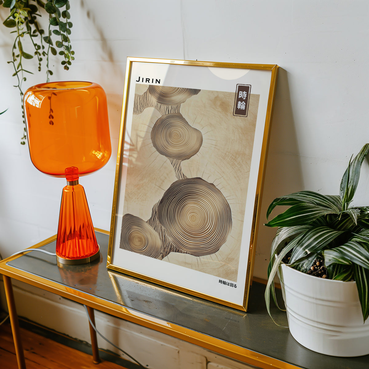Stacked beige tree ring slices print shown in a gold frame on a console beside an orange glass lamp