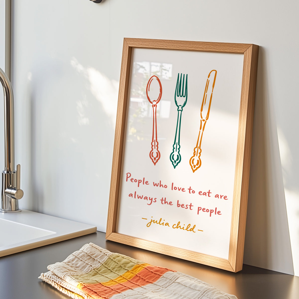 Julia Child quote print in an oak frame by the kitchen sink beside a striped tea towel