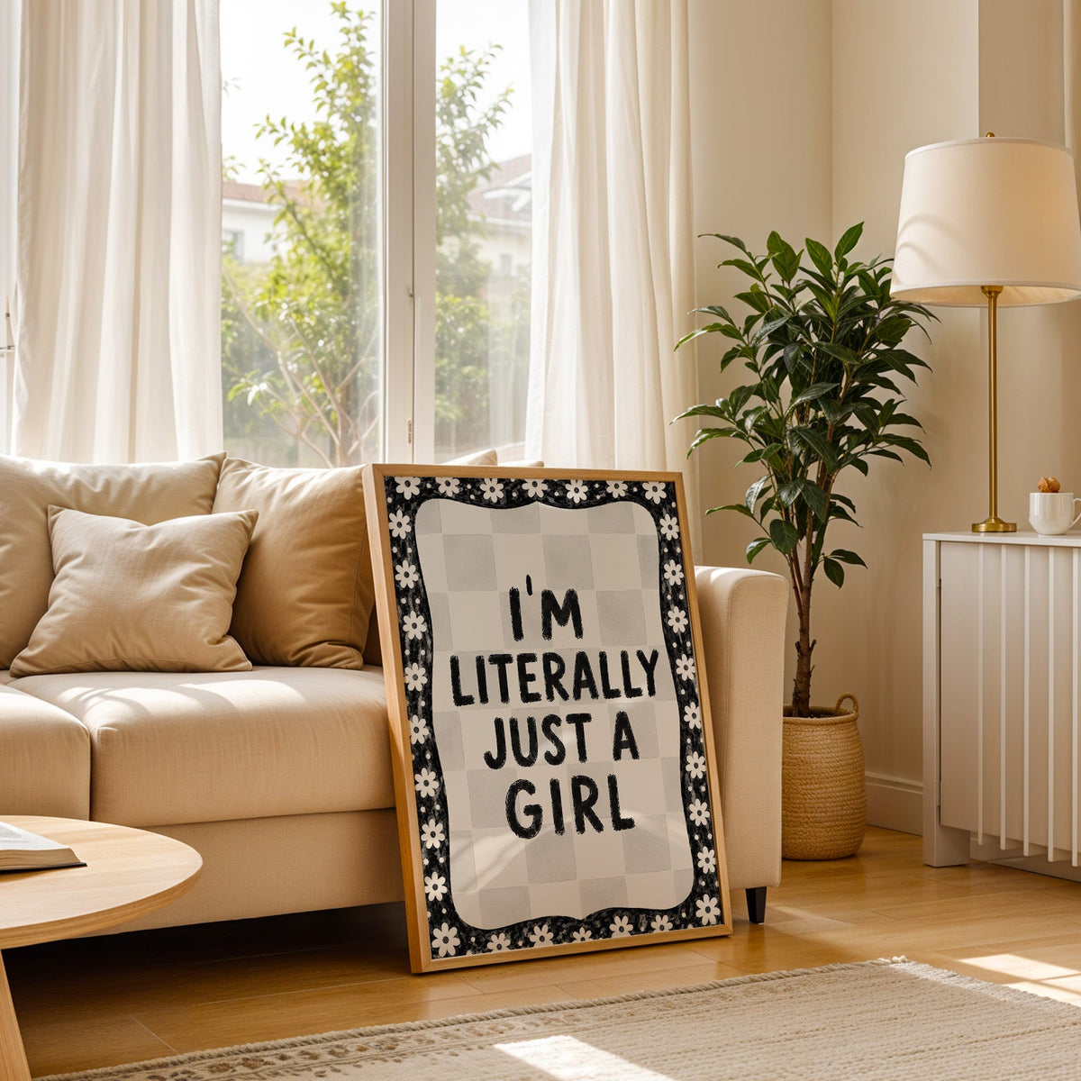 I'm literally just a girl quote with daisy border print in a light oak frame leaning on a cream sofa beside a floor lamp